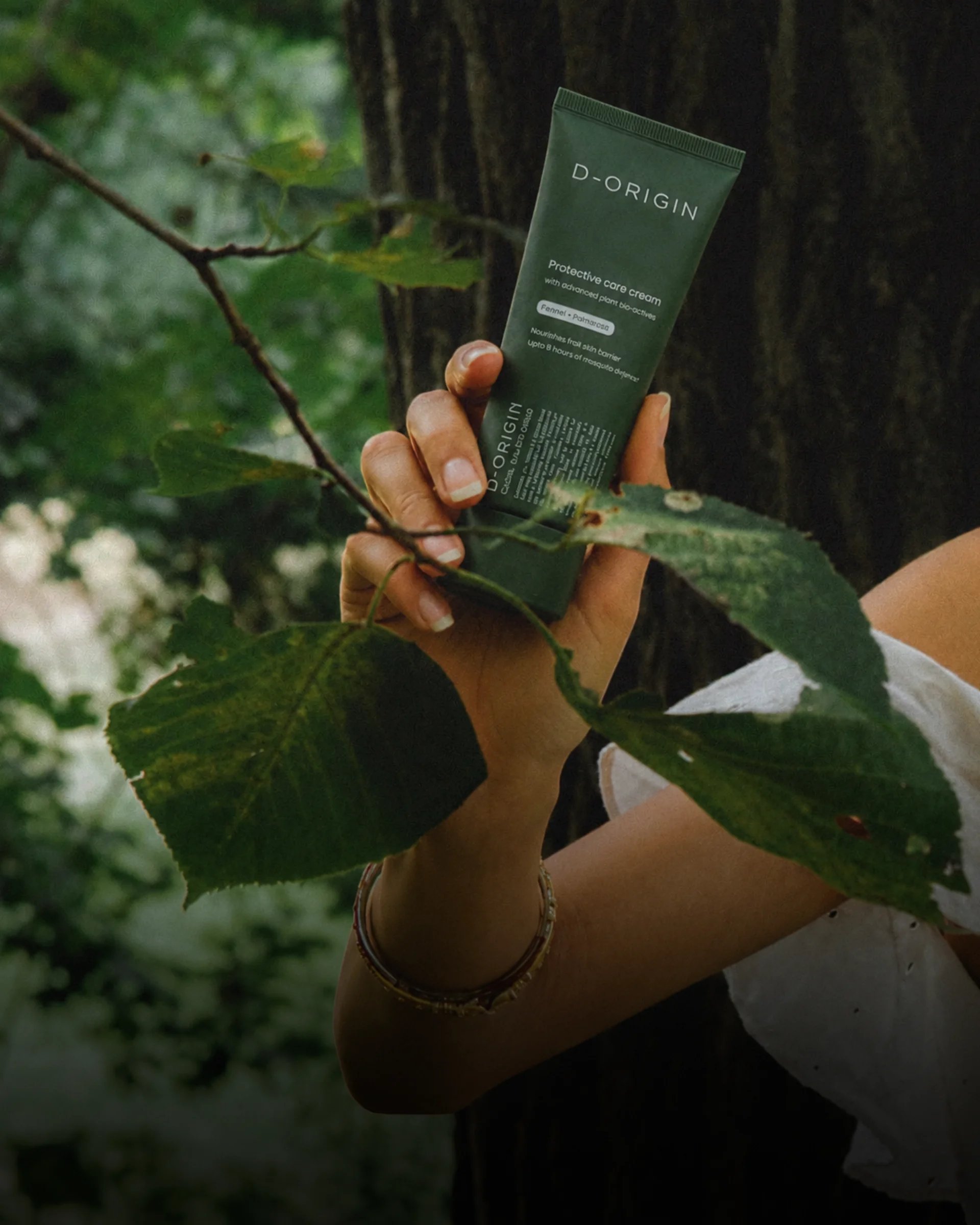 Hand holding D-Origin Protective Care Cream outdoors
